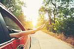 Das Bild zeigt eine Hand die aus einem Autofenster gestreckt wird auf einer sommerlichen Straße 